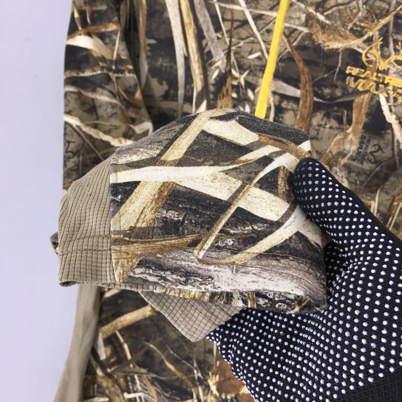 Puede incluir: Chaqueta con estampado de camuflaje en marr&oacute;n, beige y blanco. La chaqueta tiene un pu&ntilde;o acanalado y una cremallera amarilla. El logotipo de Realtree Max es visible en la parte superior derecha.