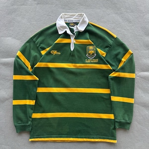 May include: A long-sleeve rugby shirt featuring horizontal green and yellow stripes, a white collar, and a button placket. The chest displays a gold kangaroo logo and a crest with the text St. John's College Sydney University embroidered in yellow.