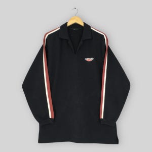 May include: Black long-sleeve shirt with a collared neckline and a small logo. The shirt features white and maroon stripes down the sleeves. The shirt is hanging on a wooden hanger.