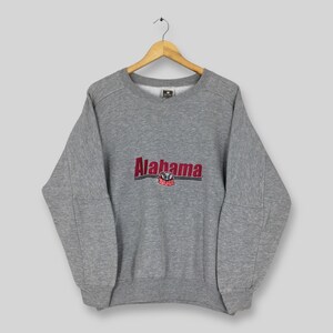 May include: A heather gray sweatshirt with the word "Alabama" in red and black lettering across the chest. Below the word "Alabama" is a graphic of a crimson elephant. The sweatshirt is hanging on a wooden hanger.
