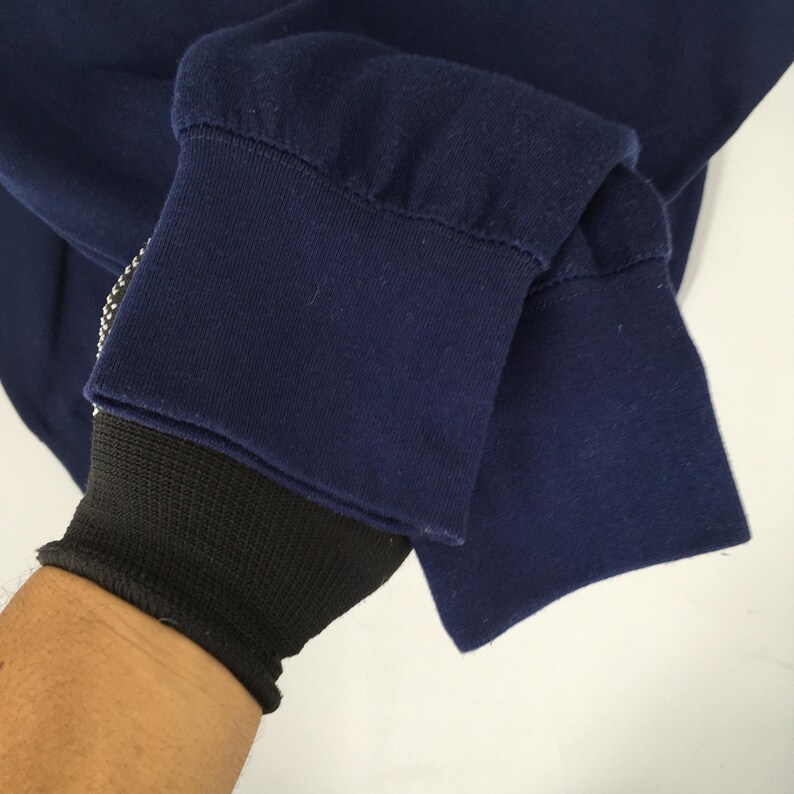 Op de afbeelding: Close-up van een marineblauwe sweatshirtmouw. De manchet is omgeslagen en onthult een zwarte geribbelde gebreide polsband. De stof is effen donkerblauw.