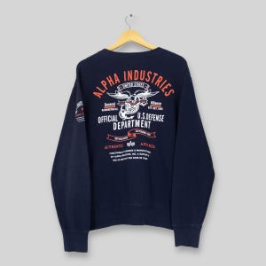 Puede incluir: Sudadera azul marino de Alpha Industries con un gráfico en la espalda que dice "Alpha Industries United States Official U.S. Defense Department". La sudadera tiene cuello redondo y mangas largas.