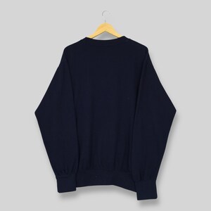 Op de afbeelding: Een marineblauw sweatshirt hangt aan een houten hanger. Het sweatshirt heeft een ronde hals en lange mouwen. De manchetten en zoom zijn geribbeld. De achtergrond is lichtgrijs.