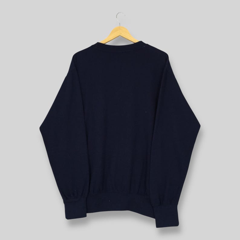 Op de afbeelding: Een marineblauw sweatshirt hangt aan een houten hanger. Het sweatshirt heeft een ronde hals en lange mouwen. De manchetten en zoom zijn geribbeld. De achtergrond is lichtgrijs.