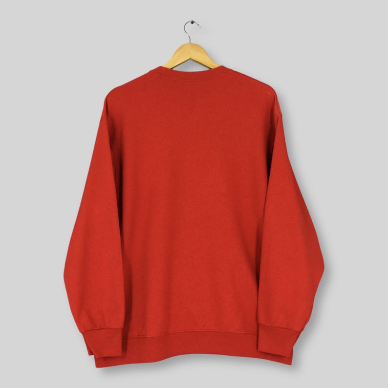 May include: A solid red sweatshirt hangs from a wooden hanger. The long-sleeved top has a crew neck and ribbed cuffs and hem. The garment is made of a soft material.