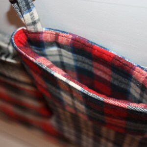 May include: A red, white and blue plaid stocking with a white cuff and a black trim. The stocking is hanging from a hook.