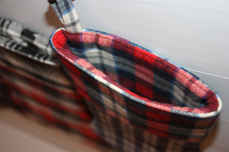 May include: A red, white and blue plaid stocking with a white cuff and a black trim. The stocking is hanging from a hook.