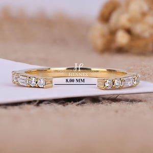 May include: A gold open-style ring featuring alternating baguette and round-cut clear stones on both ends. The band displays the text Hennes and 8.00 MM, indicating a measurement of 8.00 mm for the open gap between the two stone-set ends.