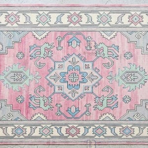 K&ouml;nnte beinhalten: Rechteckiger Teppich mit rosa Mittelfeld und cremefarbenem Rand. Geometrische Muster in Blau, Grau und Mintgr&uuml;n. Die Kanten haben Fransen. Der Teppich ist f&uuml;r die Inneneinrichtung im traditionellen Stil konzipiert.