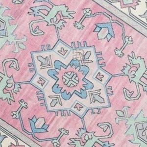K&ouml;nnte beinhalten: Nahaufnahme eines rosa gemusterten Teppichs mit einem sternf&ouml;rmigen Mitteldesign. Der Teppich weist ein sich wiederholendes geometrisches Muster in Rosa-, Blau- und Gr&uuml;nt&ouml;nen auf. Das Design wird von einem hellgrauen Rand umrahmt.