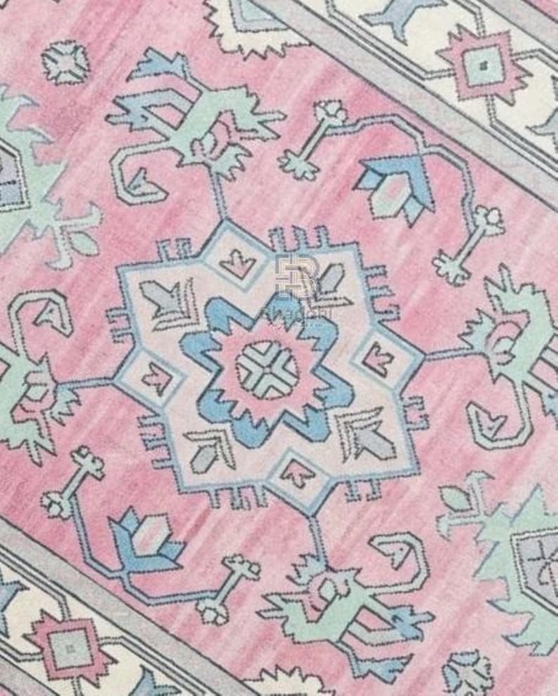 K&ouml;nnte beinhalten: Nahaufnahme eines rosa gemusterten Teppichs mit einem sternf&ouml;rmigen Mitteldesign. Der Teppich weist ein sich wiederholendes geometrisches Muster in Rosa-, Blau- und Gr&uuml;nt&ouml;nen auf. Das Design wird von einem hellgrauen Rand umrahmt.