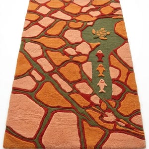 May include: A rectangular area rug featuring a textured, stone-like pattern in shades of orange, peach, and dark red, separated by dark green lines. A green section on the right side contains a small turtle and three fish in red, orange, and peach.