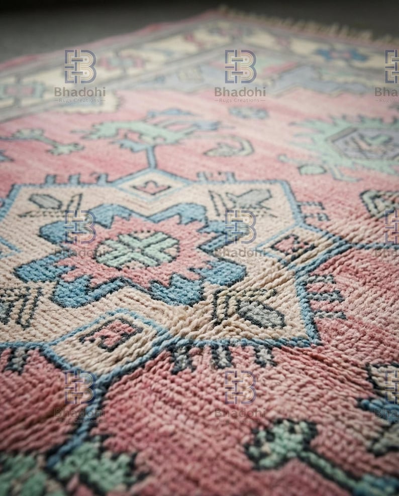 K&ouml;nnte beinhalten: Nahaufnahme eines handgewebten Teppichs mit detailliertem geometrischem Muster. Der Teppich hat eine Farbpalette aus Rosa, Blau und Creme. Die Textur des Teppichs ist sichtbar und zeigt die komplizierte Webart und das Design.