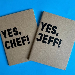 Może przedstawiać: Dwa brązowe zeszyty z nadrukowanym czarnym tekstem "YES, CHEF!" i "YES, JEFF!"