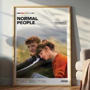 Puede incluir: Un póster enmarcado con el título "NORMAL PEOPLE" en texto negro. El póster presenta una fotografía de un hombre y una mujer, con la mujer apoyando la cabeza en el hombro del hombre. El póster se exhibe en una habitación con una lámpara y una silla.