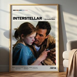 Peut inclure: Affiche encadrée du film "Interstellar" représentant un homme et une fille dans une étreinte. L'affiche a un design minimaliste avec le titre du film et le nom du réalisateur. Le cadre est de couleur claire et l'affiche est exposée dans une pièce aux couleurs neutres.