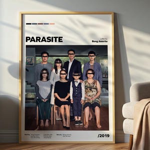 Pode incluir: Um cartaz de filme emoldurado para "Parasite" com um grupo de pessoas usando óculos de sol. O cartaz tem uma moldura de madeira clara e é exibido em uma sala com um esquema de cores neutras. O cartaz está encostado em uma parede cinza.