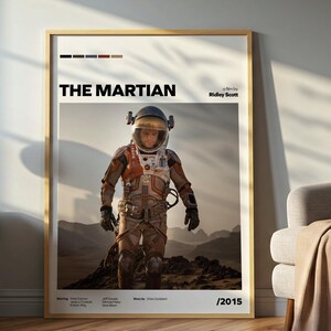 May include: A framed poster for the movie "The Martian" featuring an astronaut in a spacesuit on a rocky landscape. The poster has a gold frame and includes the film's title and director's name.