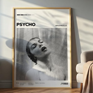 May include: A framed black and white poster of the movie "Psycho" by Alfred Hitchcock. The poster features a woman with her head tilted back, with the movie title and year, 1960, displayed prominently. The poster is in a room with a lamp and a chair.