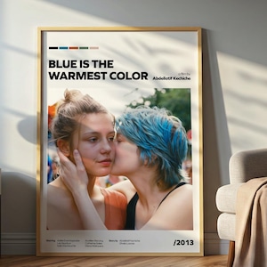 May include: A rectangular wall poster in a light wood frame featuring the film title Blue Is The Warmest Color, directed by Abdellatif Kechiche, with a color palette bar at the top and the year 2013 at the bottom, displaying two people embracing.