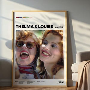 Puede incluir: Un póster enmarcado de la película "Thelma & Louise" con una foto de las dos actrices principales. El póster tiene un borde beige e incluye el título de la película y el año 1991. La imagen se muestra en un entorno de habitación.