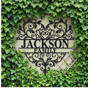 May include: Black metal family name sign with the text "JACKSON FAMILY" in a decorative font. The sign has an ornate, heart-shaped design with swirling patterns and is surrounded by green ivy.