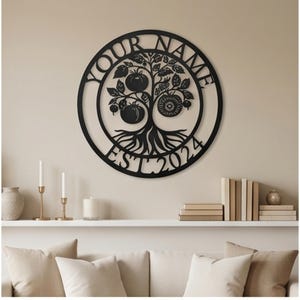 May include: A circular black metal wall art piece featuring a stylized tree with visible roots and tomato-like fruits. The text "YOUR NAME" is arched across the top, and "EST. 2024" is positioned along the bottom edge of the circular frame.