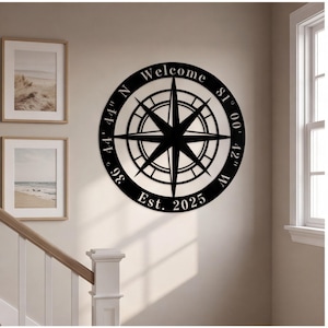 May include: A circular black metal wall sign featuring a central compass rose design. The outer ring displays the text Welcome, the coordinates 36 44' 44" N 81 00' 42" W, and the text Est. 2025 in a white serif font against the black metal surface.