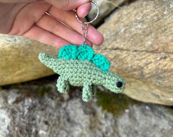 May include: Green crocheted dinosaur keychain with a black eye and a silver key ring.