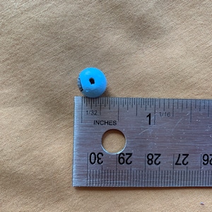 Puede incluir: Una cuenta de madera azul claro que mide aproximadamente 1,25 cm de di&aacute;metro. La cuenta est&aacute; al lado de una regla para referencia de tama&ntilde;o.