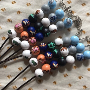 Puede incluir: Un conjunto de cuentas de madera de colores con varios dise&ntilde;os, incluyendo &aacute;rboles, animales y formas geom&eacute;tricas. Las cuentas est&aacute;n enhebradas en cordones negros y algunas tienen cierres plateados.