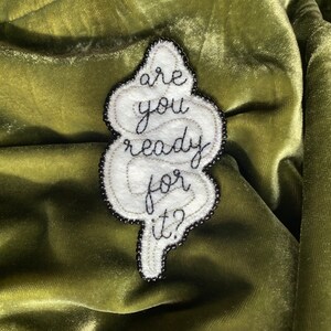 May include: White felt patch with black embroidery that reads "are you ready for it?" The patch is shaped like a cloud and is surrounded by black beads.