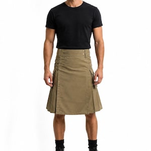 Op de afbeelding: Een kaki kilt met plooien en zakken, gecombineerd met een zwart t-shirt en zwarte laarzen. De kilt heeft een traditioneel ontwerp met een knoopsluiting en zijbanden. Het model staat tegen een witte achtergrond. De lengte van de kilt is ongeveer 50 cm.