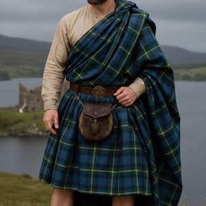 Puede incluir: Un hombre con vestimenta tradicional escocesa, incluyendo un kilt a cuadros azul y verde y un chal a juego. Lleva un cinturón de cuero marrón con una hebilla decorativa, un sporran y calcetines marrones. El fondo muestra un lago y un castillo.