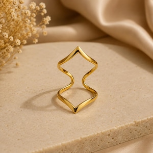 May include: A gold-toned ring featuring a double chevron or zigzag design. The band is composed of two connected V-shaped segments that create an open, geometric silhouette with smooth, polished surfaces and a reflective metallic finish.