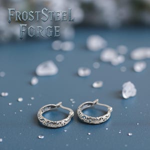 Könnte beinhalten: Ein Paar silberner Creolen mit einem aufwendigen, wirbelnden Design. Die Ohrringe werden auf einer blauen Oberfläche präsentiert, mit dem Text "FrostSteel Forge". Der Hintergrund zeigt kleine, weiße, eisähnliche Formen.