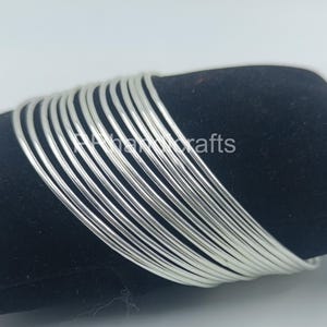 May include: A set of twelve thin, polished silver-colored bangles arranged in a stack. The circular bracelets feature a smooth, reflective metallic surface and a simple, uniform design. The text "PHhandcrafts" is visible across the center of the bangles.