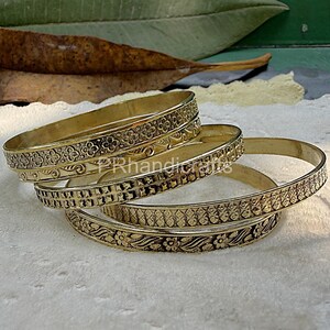 May include: Four gold-colored bangles with intricate floral and geometric patterns. The bangles are stacked on top of each other, showcasing the detailed designs. The bangles are made of metal and have a shiny finish.