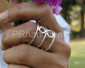 May include: A silver ring with an infinity symbol design. The ring has a delicate, minimalist style. The image also shows a hand holding purple flowers. The text "PRhangcrafts" is visible.