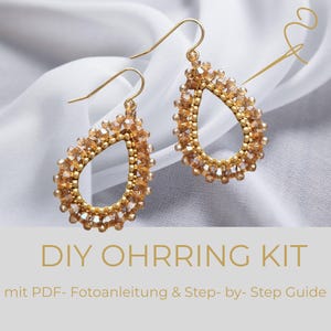 May include: A pair of teardrop-shaped earrings featuring gold-toned beads and light brown crystals with gold hooks. The text DIY OHRRING KIT mit PDF- Fotoanleitung & Step- by- Step Guide is printed below the earrings on a light grey background.