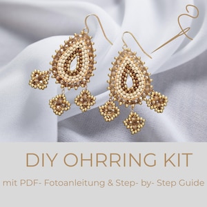 Könnte beinhalten: Ein Paar tropfenförmige Perlenohrringe mit cremefarbenen und bronzefarbenen Perlen und drei hängenden quadratischen Perlenanhängern. Die Ohrringe haben goldfarbene Haken. Der Text DIY OHRRING KIT mit PDF- Fotoanleitung & Step- by- Step Guide ist sichtbar.