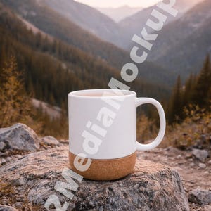 May include: A white ceramic mug with a cork base sits on a rock in a mountain setting. The mug has a simple design and a curved handle. The background features a scenic view of mountains and trees, with a warm, natural color palette.