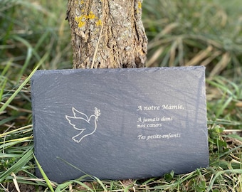 May include: A rectangular, dark gray slate plaque with a dove illustration and French text. The dove is holding an olive branch. The text reads "A notre Mamie, A jamais dans nos coeurs, Tes petits-enfants."