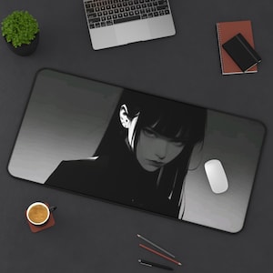 May include: A rectangular mouse mat with a black and white illustration of a woman with long black hair. The mat is on a dark surface, with a white mouse and other office supplies. The image is in grayscale.