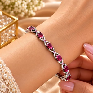 Peut inclure: Un bracelet aux tons argentés composé d'une série de pierres précieuses ovales rose foncé disposées en motif répétitif. Les maillons métalliques entre les pierres forment une croix entrelacée, ornée de petites pierres rondes rose clair.
