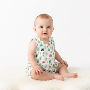 May include: A sleeveless baby romper featuring a white background with a repeating pattern of small brown bears, green trees, and blue geometric shapes. The garment has a V-neckline and a loose, comfortable fit suitable for an infant's daily wear.