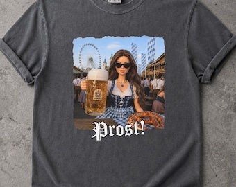 May include: A charcoal gray short-sleeve t-shirt featuring a graphic print of a doll wearing a blue and white dirndl, holding a large glass beer mug and a pretzel. The background shows a fairground scene with a Ferris wheel. The text Prost! is below.