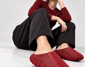 Könnte beinhalten: Ein Paar dunkelrote Schlupfschuhe mit einer dicken, geriffelten Sohle und einem strukturierten, perforierten Obermaterial. Das Schuhwerk hat eine abgerundete Zehenpartie und eine einfarbige, matte Oberfläche in einem robusten Design.