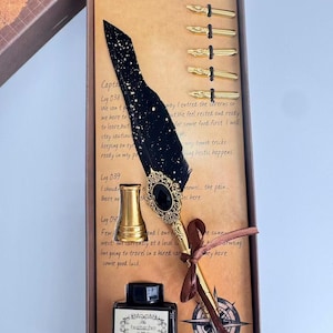 May include: A calligraphy set in a rectangular box containing a black feather quill pen with gold speckles, a gold-toned metal handle with a black oval inlay, five gold-toned metal nibs, a gold-toned pen stand, and a square glass ink bottle.