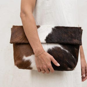 Handcrafted large leather clutch bag made from genuine tri-color hair-on-hide cowhide, featuring a modern foldover design in natural brown, black, and white tones for a western boho aesthetic. gift for her, gift for sister, gift for mother, personalized gift, custom handmade gift, trendy fashion